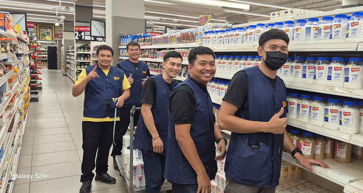 עובדים תאילנדים בסניף יוחננוף רמת השרון. חמישה עובדים עם בגד של יוחננוף ליד מדף של מצרכים.
