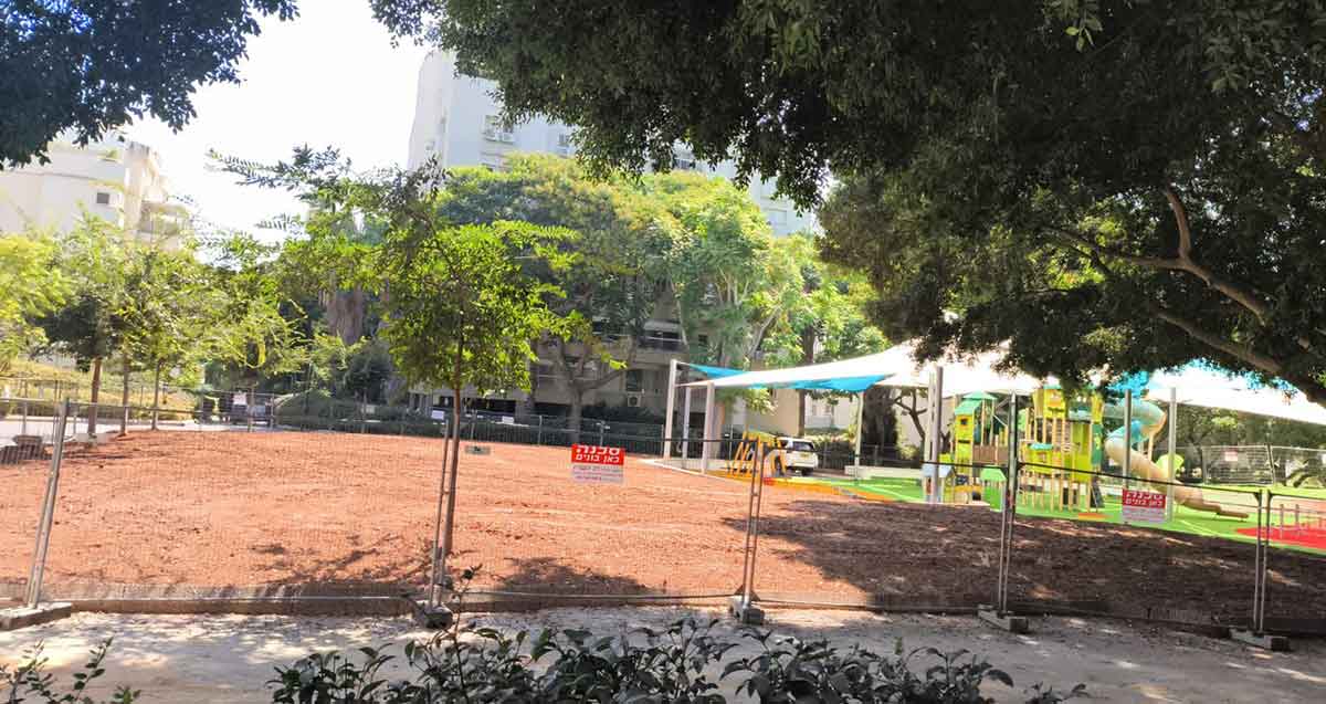 גינת אלתרמן בכפר סבא. רחבה גדולה עם גידור וכולה חול. מימין גגון בד לצל ותחתיו מגלשה ומתקן שעשועים.
