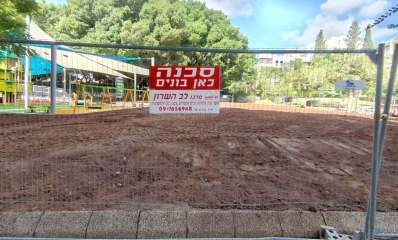 גינת אלתרמן בכפר סבא. שטח עם חול מגודר. ושלט בכיתוב: סכנה כאן בונים