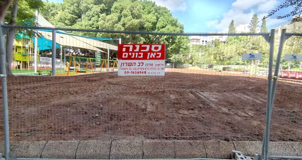 גינת אלתרמן בכפר סבא. שטח עם חול מגודר. ושלט בכיתוב: סכנה כאן בונים