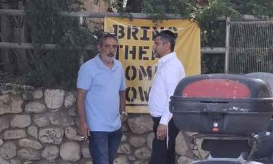 עמוס מגוז מסתודד עם זכי טיירי. ברקע שלט צהוב באנגלית: BRING THEM HOME NOW