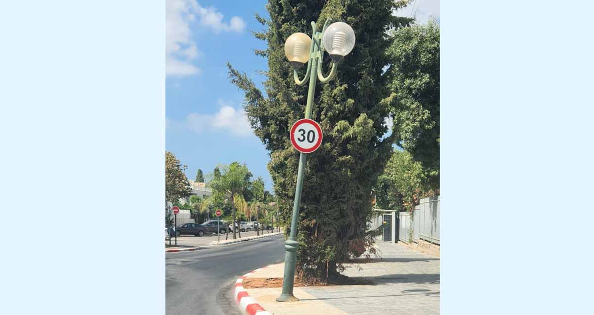 עמוד תאורה בסכנת נפילה צמוד לכיכר בית ספר השחר. על העמוד תלוי תמרור הגבלת מהירות ל 30