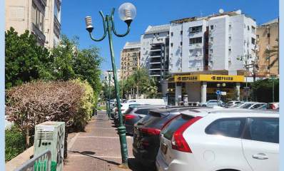 עמוד תאורה עקום בפינת הרחובות הדרור והבנים בהוד השרון. נטוע על מדרכה ליד חניית רכבים