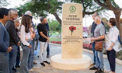 אנדרטה לנרצחי השבעה באוקטובר וקהל משני הצדדים. הכיתוב: שבעה באוקטובר, לזכרם של הנרצחים והחללים בני ובנות העיר רמת השרון. תמונה של כלנית ומתחתה הכיתוב: "שדה הקרב יהפוך לשיבולים, אנשים יפים ימשיכו לרקוד במרחבים, יכתבו כאן ספרים, ואלפי כלניות יכסו את השנים" אסי סתיו