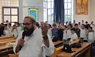 ישיבת בני עקיבא רעננה. מורה עומד עם מיקרופון ואחריו עומדים תלמידים בשורות.