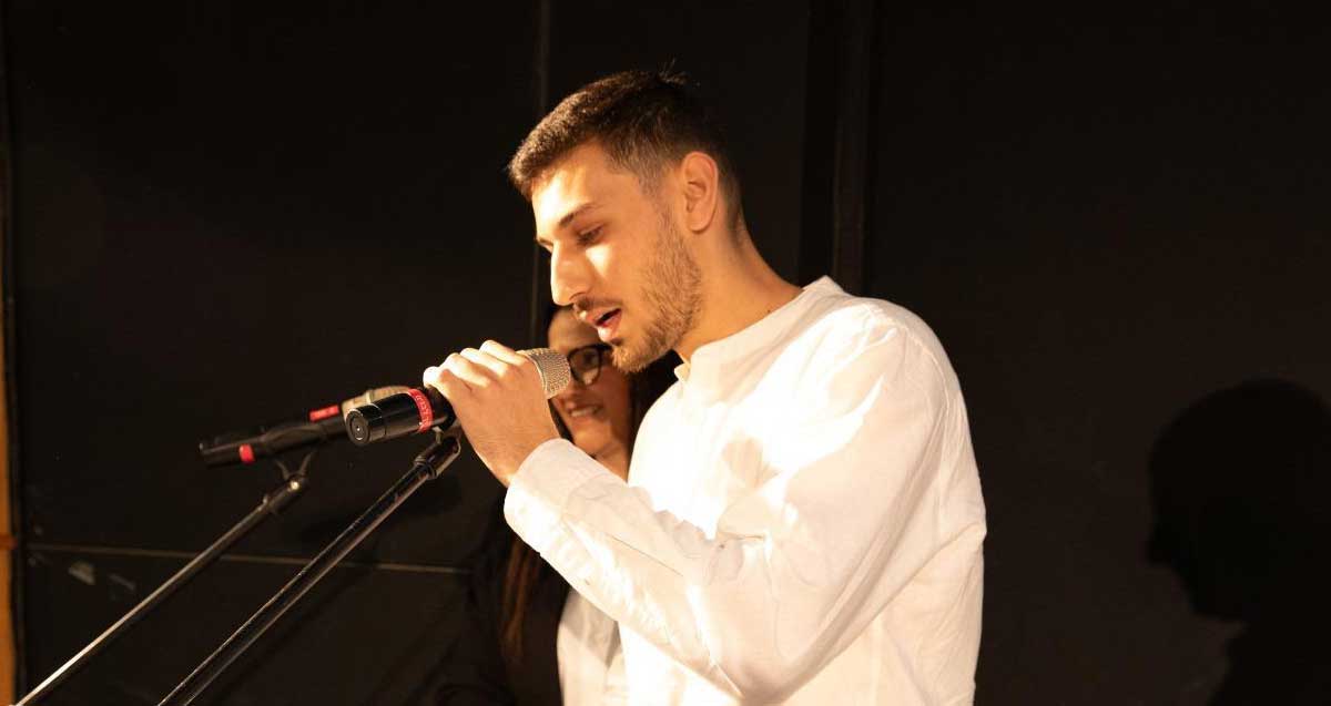 דן רוק נואם ואוחז בידו מיקרופון על חצובה