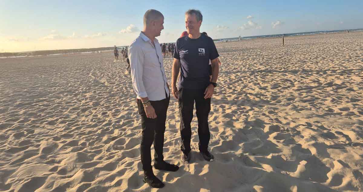 עופר לוי ויובל עילם עומדים בחוף הים. ברקע חבורת נערים.