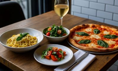 שולחן במסעדה עם מנת פסטה, סלט ופיצה וכוס יין לבן, הדמיית בינה מלאכותית: השרון אונליין