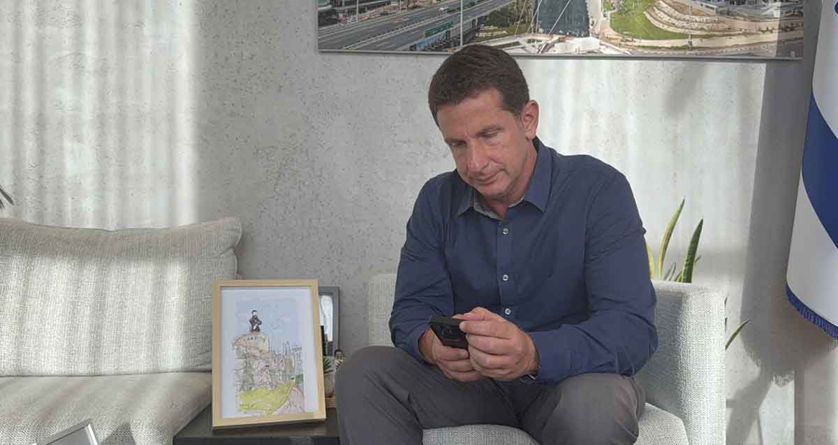 יריב פישר יושב ומתבונן בטלפון שבידיו.