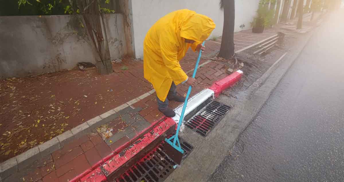 ניקוי פתחי ניקוז ברעננה. עובד עם מעיל גשם צהוב מנקה עם מטאטא.