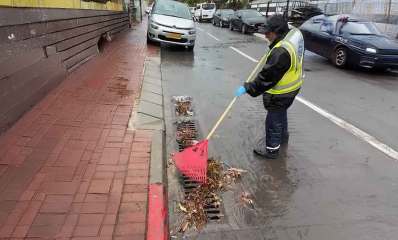 עובד עירייה מנקה פתחי ניקוז. אוסף עלים וענפים בעזרת מגרפה.