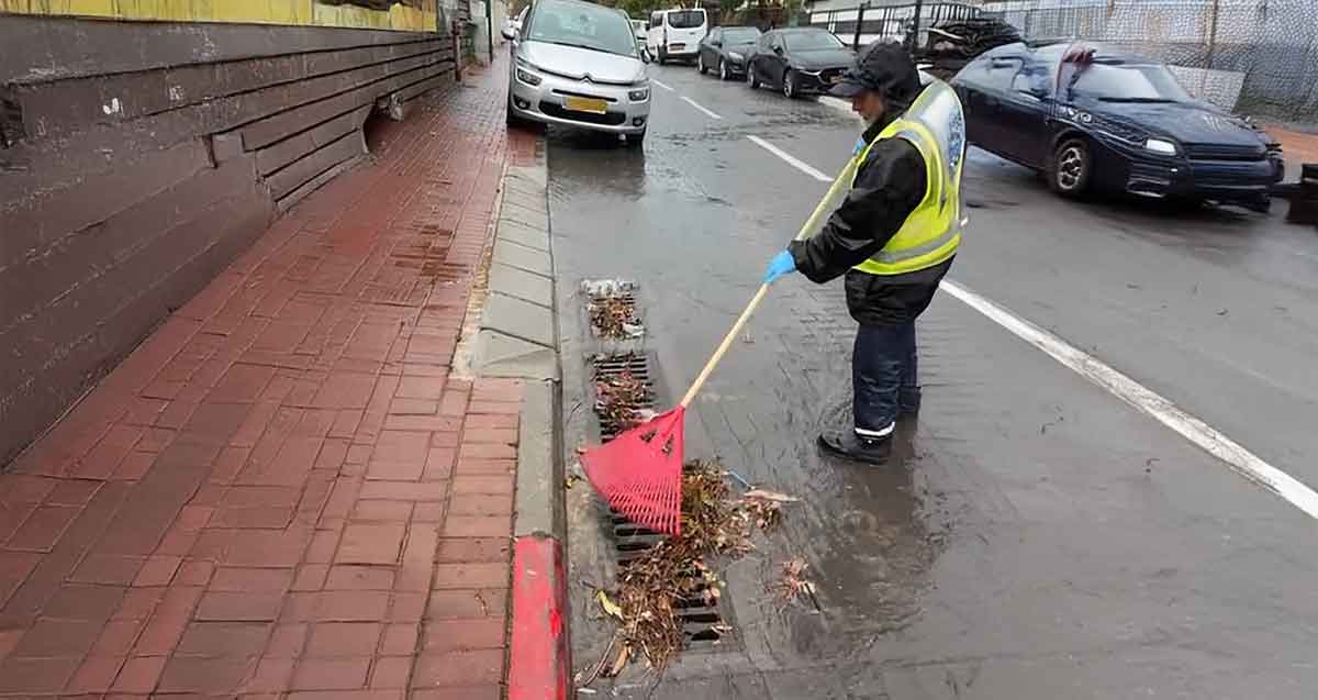עובד עירייה מנקה פתחי ניקוז. אוסף עלים וענפים בעזרת מגרפה.