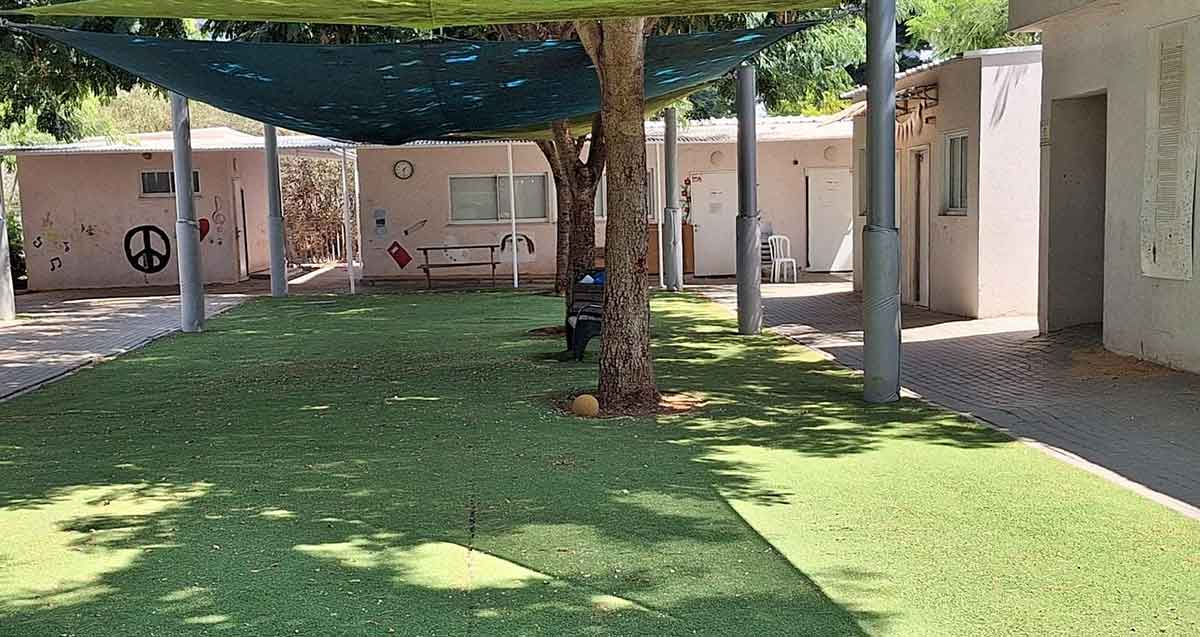 בית הספר הדמוקרטי ע"ש יאנוש קורצ'אק בהרצליה. מבנים חד קומתיים בצורת האות ר' ולפניהם רחבה עם דשא סינטטי ומעליה יריעת בד כחולה לצל.