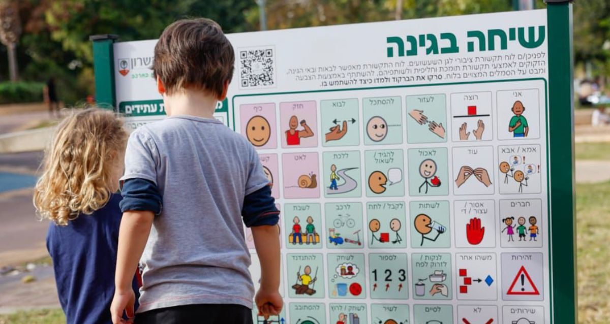 שני ילדים קטנים עומדים מול לוח תקשורת עליו יש סמלים שונים, צילום: עיריית הוד השרון