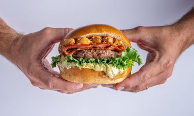 ידיים של גבר מחזיקות המבורגר דנבר של בורגר סטיישן בלחמנייה עם ירקות ותוספותף צילום: ליאור אשכנזי