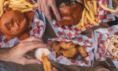 מבט על על שולחן עם מפה לבנה ואדומה מנות המבורגר נאגטס וצ'יפס וידיים של סועדים, צילום: מייסון בורגר