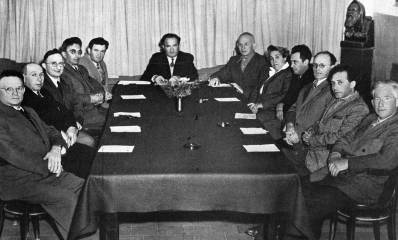 תמונה ישנה שחור לבן של ישיבת המועצה המקומית בכפר סבא בראשות סוקיס. 11 גברים ואישה אחת יושבים סביב שולחן