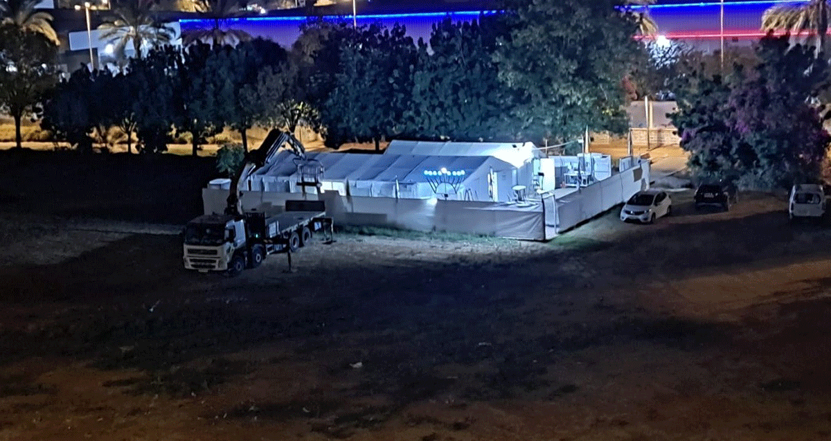 מתחם אוהל בית הכנסת בכפר סבא. מכוסה בשתי יריעות בד לבנות. ליד הגדר חנוכייה.