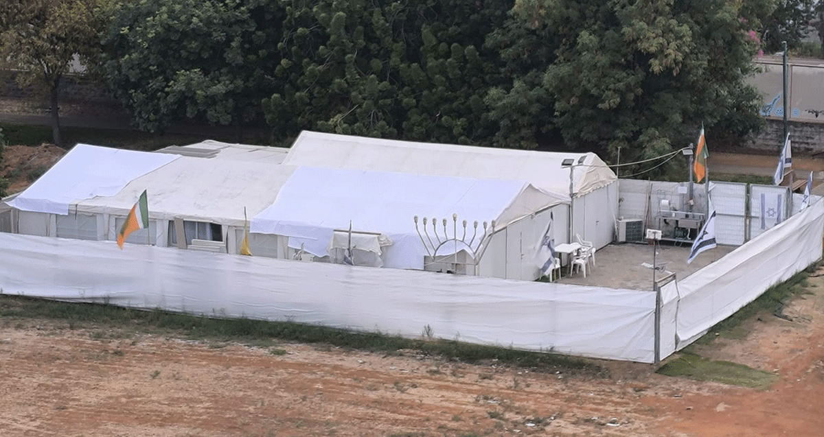 מתחם אוהל בית הכנסת בכפר סבא. מכוסה בשתי יריעות בד לבנות. ליד הגדר חנוכייה.