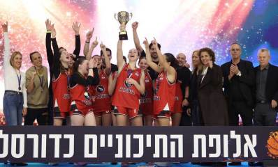 נבחרת הבנות בכדורסל של תיכון רוטברג מניפה את הגביע, וכיתוב: אלופת התיכוניים כדורסל. מסביב לבנות נשים וגברים.