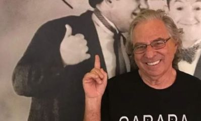 נחום לנגסם מחייך ומצביע על איור קיר מאחוריו, צילום: פרטי