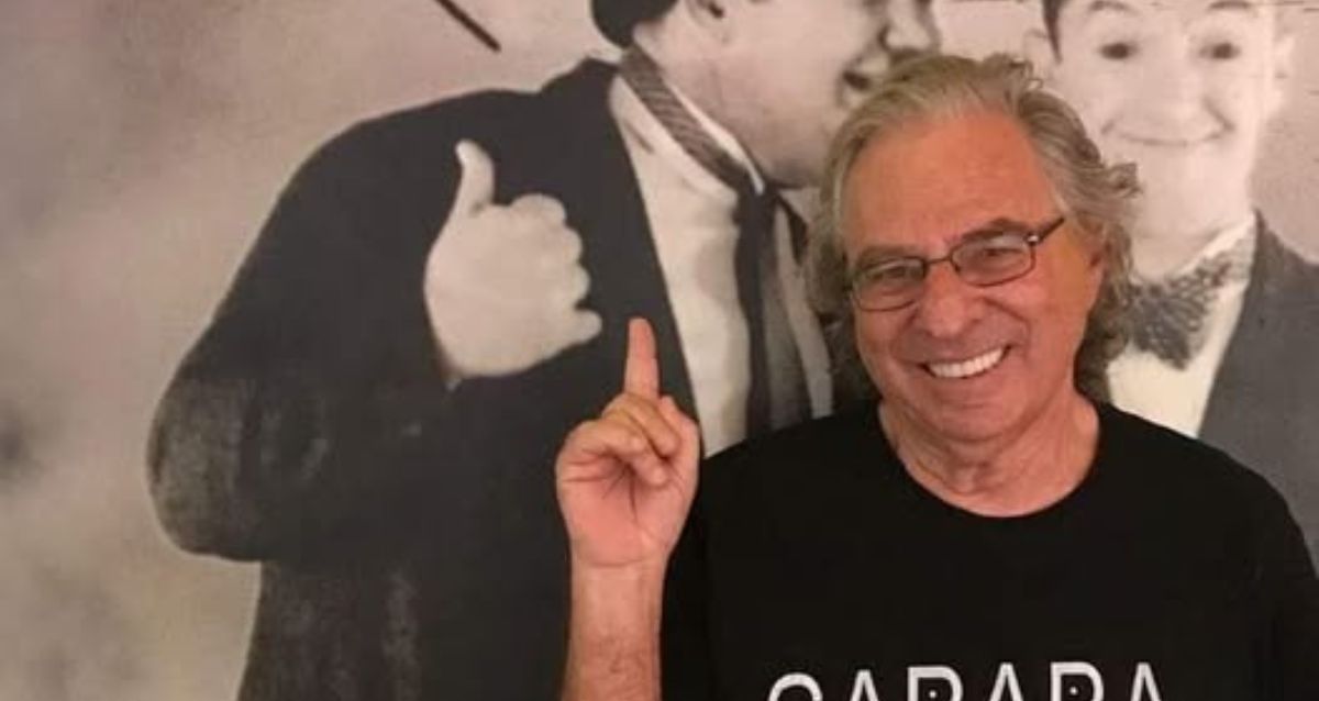 נחום לנגסם מחייך ומצביע על איור קיר מאחוריו, צילום: פרטי