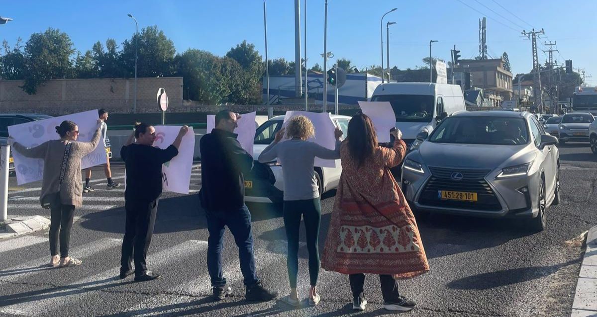 צילום מהגב של הורים העומדים במעבר חציה, הם מחזיקים שלטים ומולם מכוניות, צילום פרטי