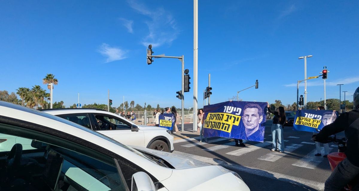 הורים עומדים עם שלטים של הפגנה על מעבר חצייה לפניהם מכוניות פרטיות. צילום: פרטי