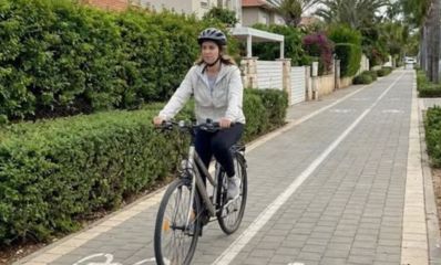 איזה רוכבת עם קסדה על שביל אופניים ברקע בתים פרטיים, הדמיית בינה מלאכותית: עיריית רמת השרון