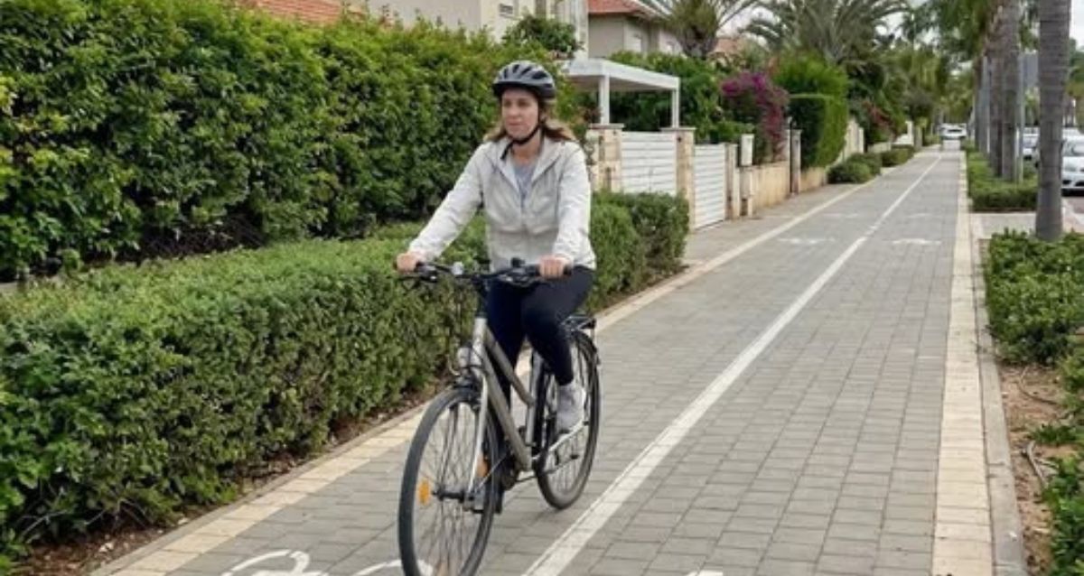 איזה רוכבת עם קסדה על שביל אופניים ברקע בתים פרטיים, הדמיית בינה מלאכותית: עיריית רמת השרון
