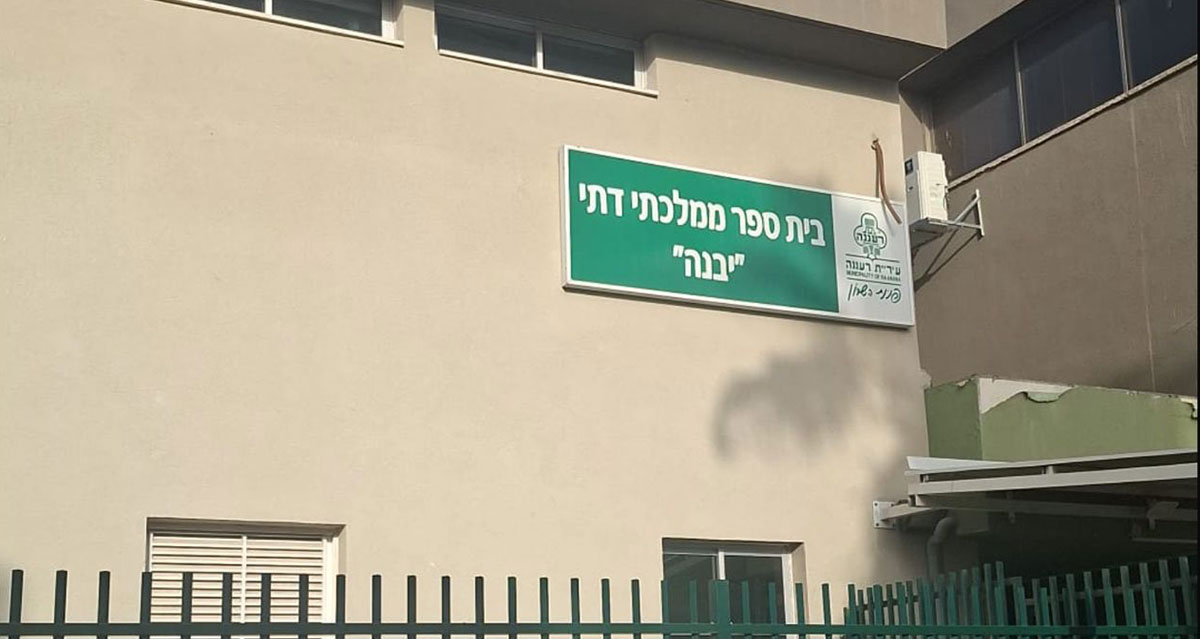קיר חזית המבנה בית הספר הממלכתי דתי יבנה ברעננה. השלט מתנוסס על הקיר