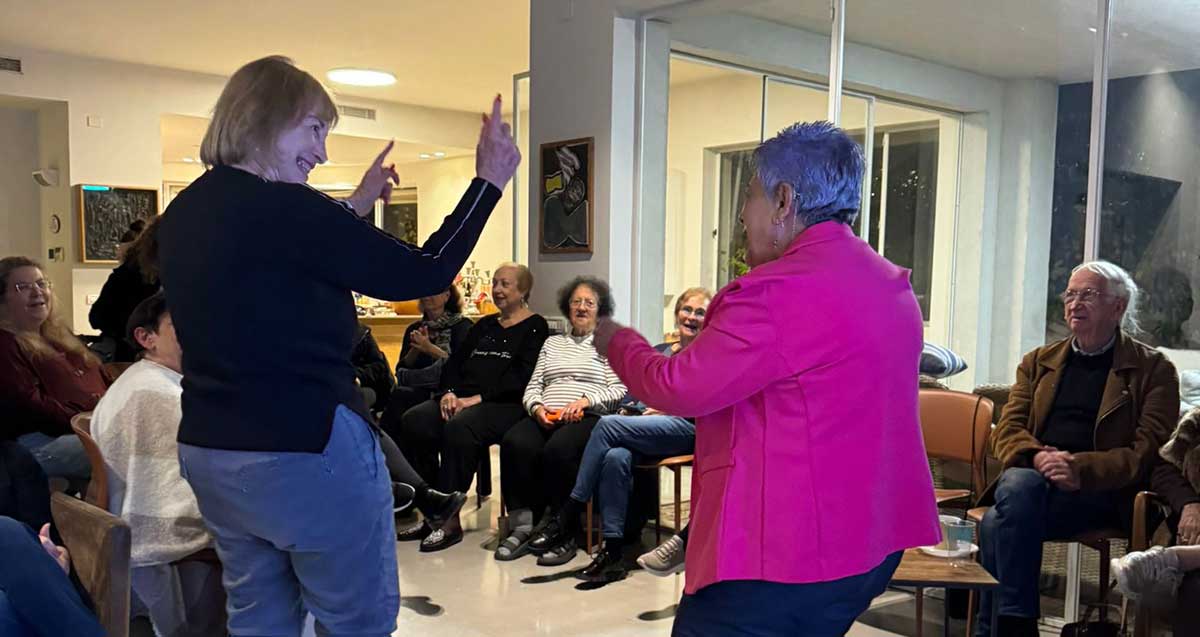 מפגש גיל שלישי. שתי נשים רוקדות מול נשים וגברים היושבים בשתי שורות של כסאות.