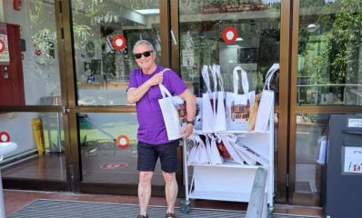 איש ע חולצה סגולה נושא על הכתף תיק ספרייה, מאחורי עגלה עם שקיות וספרים, צילום: עיריית כפר סבא