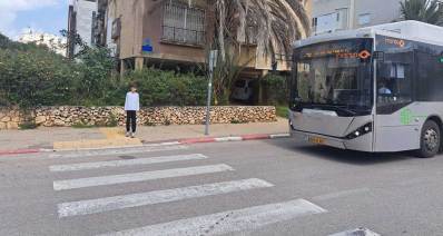 אוטובוס ברחוב הבנים בהרצליה. האוטובוס עוצר ליד מעבר חצייה וילד על המדרכה ליד מעבר החצייה.