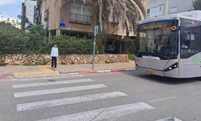 אוטובוס ברחוב הבנים בהרצליה. האוטובוס עוצר ליד מעבר חצייה וילד על המדרכה ליד מעבר החצייה.