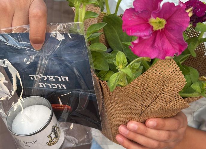 ידיים מחזיקות עציץ ונר יזכור, צילום: עיריית הרצליה 