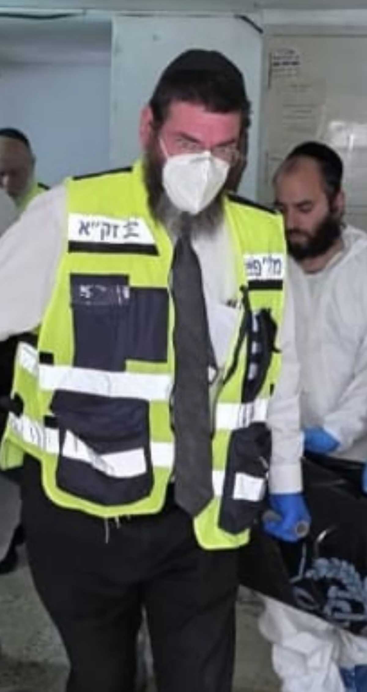 הרב יצחק אדלשטיין עם אפוד של זק"א ומסכת פנים אוחז באלונקה.