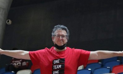 גיא ברזל לובש חולצה אדומה עליה כתוב ONE TEAM ONE. ופורש ידיו לצדדים