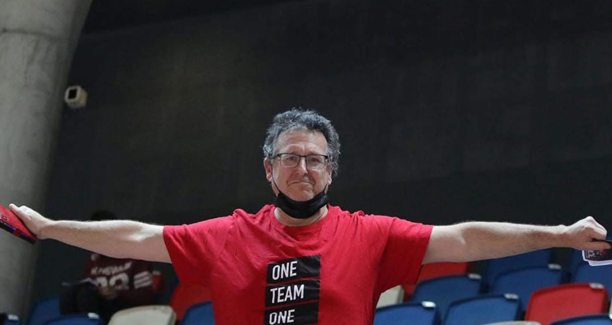 גיא ברזל לובש חולצה אדומה עליה כתוב ONE TEAM ONE. ופורש ידיו לצדדים