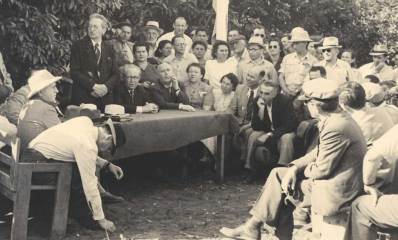 צילום שחור לבן משנת 1946 שבו יצחק בן צבי נואם ליד שולחן בשטח ומניח את אבן הפינה לחצרות הדר וסביבו קהל גברים ונשים