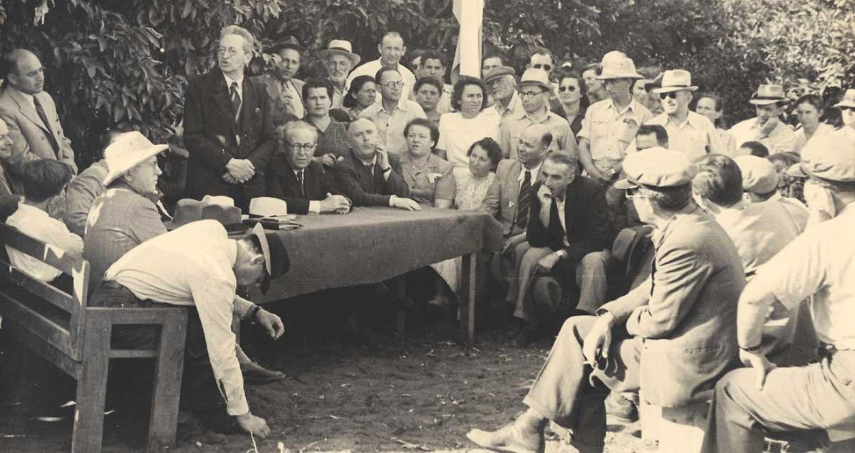 צילום שחור לבן משנת 1946 שבו יצחק בן צבי נואם ליד שולחן בשטח ומניח את אבן הפינה לחצרות הדר וסביבו קהל גברים ונשים