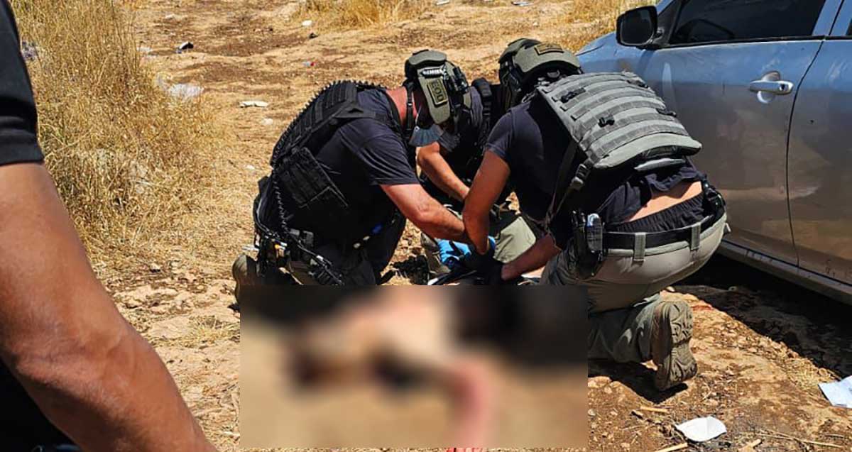 שוטרים של כוחות הביטחון רוכנים מעל אדם בשטח. האדם מטושטש
