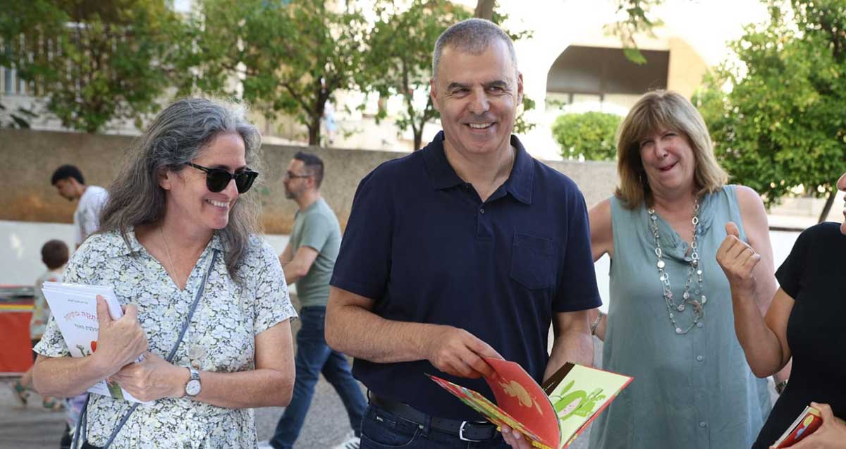 רפי סער בשבוע הספר בעיר ביוני 2026. עם ספר ילדים בידיו ואישה בכל צד שלו.