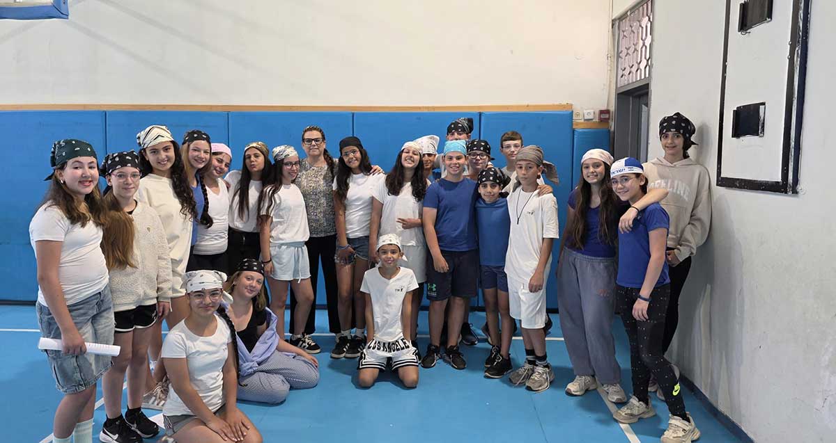 תלמידי כיתה ו' בבית הספר שז"ר, עומדים בצילום קבוצתי ושלושה תלמידים על הרצפה.