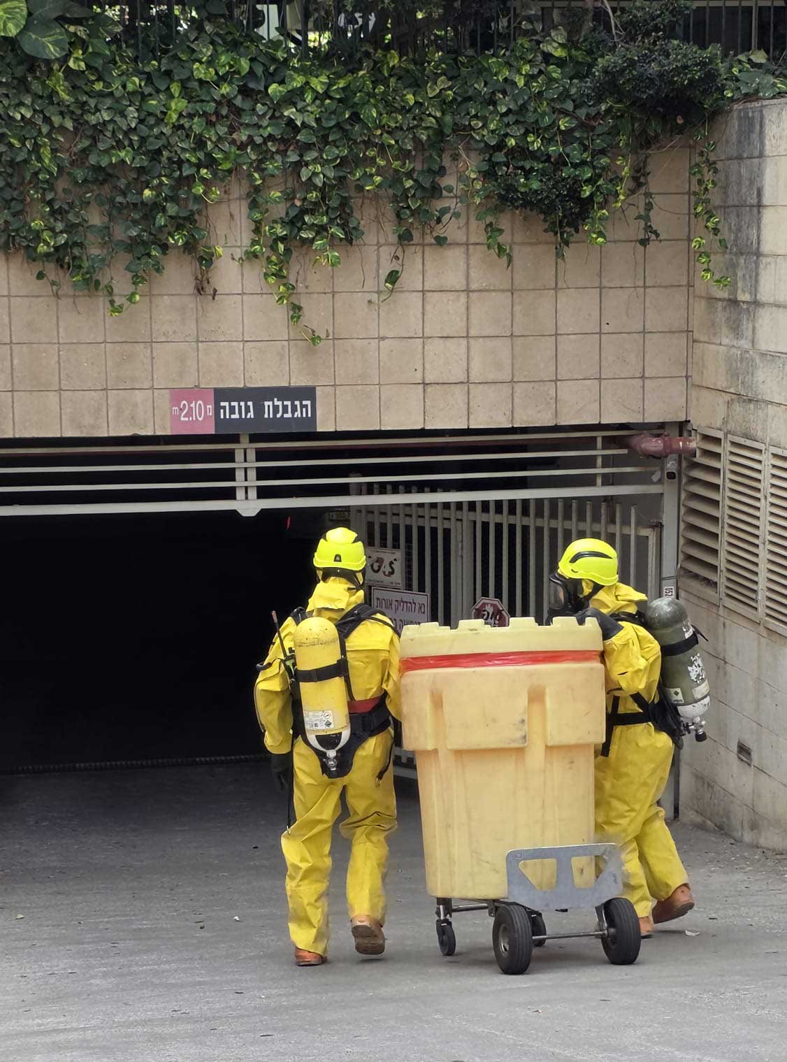 שני כבאיים עם ציוד לניטרול חומרים כימיים מובילים מיכל ענק לחניון של בניין