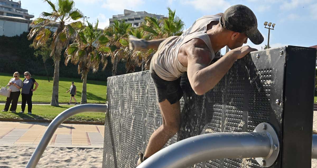נער מטפס מעל מתקן המדמה מעבר מכשול (קיר) במתחם כושר קרבי בחוף הים של הרצליה