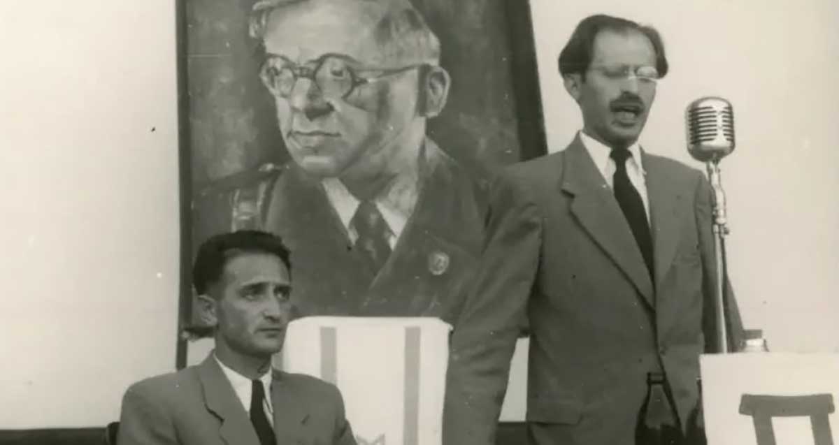 מנחם בגין נואם. מאחוריו תלויה תמונה של ז׳בוטינסקי. הצילום ישן בשחור לבן