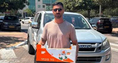 אלי שבת, מפקח ניקיון ברובע צפון. עומד לפני רכב עם קרטון בידיים ועל הקרטון כיתוב: גזר מובחר
