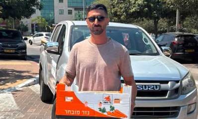 אלי שבת, מפקח ניקיון ברובע צפון. עומד לפני רכב עם קרטון בידיים ועל הקרטון כיתוב: גזר מובחר
