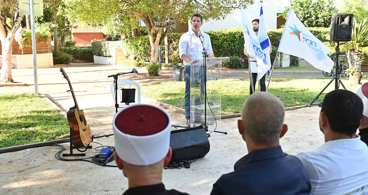 טקס חנוכת גינה ע"ש מחמוד ח'יר אלדין. ראש עיריית הרצליה ליד דוכן הנואמים ומיקרופון, לפני קהל היושב מולו.